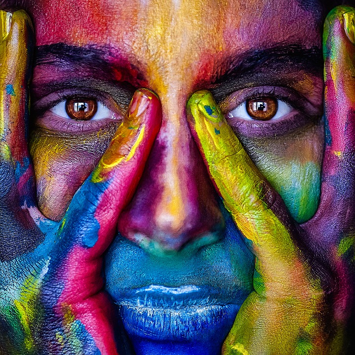 Visage peint de couleurs vives, mains levées : symbole de l'expression authentique de soi