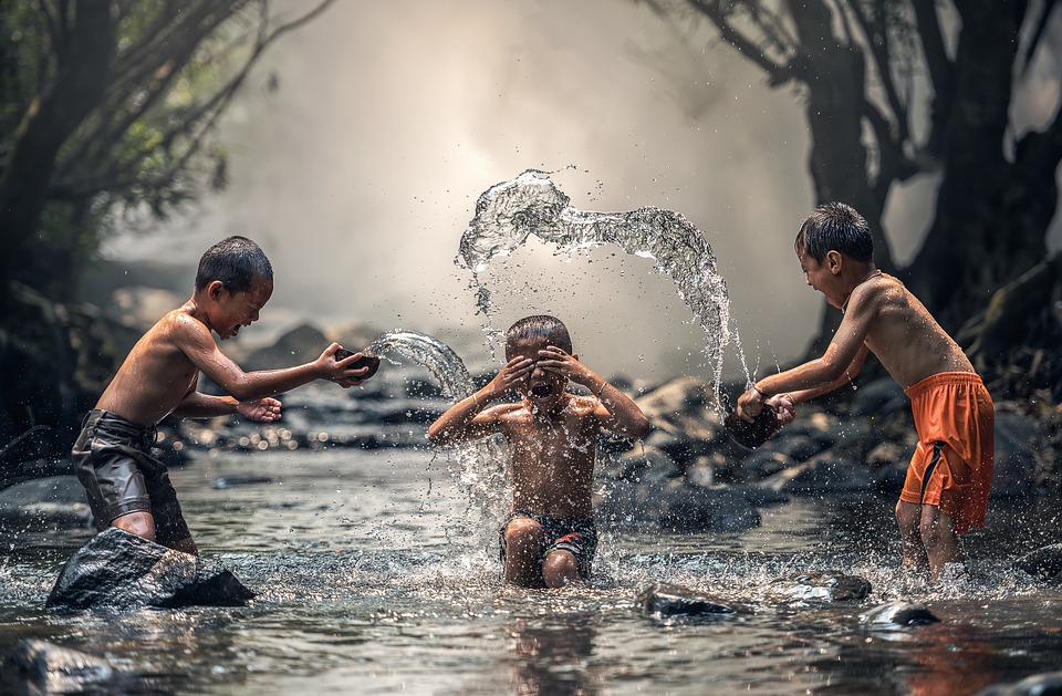 Trois enfants jouant ensemble dans une rivière, illustrant la joie et la coopération du collectif